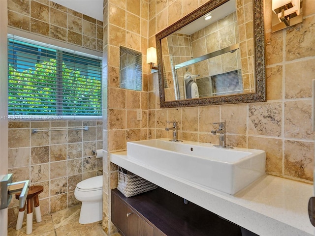 bathroom with toilet, tile patterned floors, vanity, backsplash, and tile walls