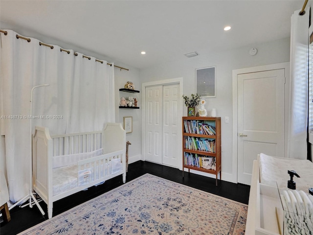 bedroom with a nursery area, dark hardwood / wood-style floors, and a closet