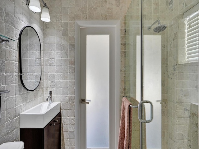 bathroom with a shower with door, vanity, toilet, and tile walls