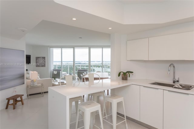 kitchen featuring a kitchen breakfast bar, light tile flooring, floor to ceiling windows, white cabinetry, and sink