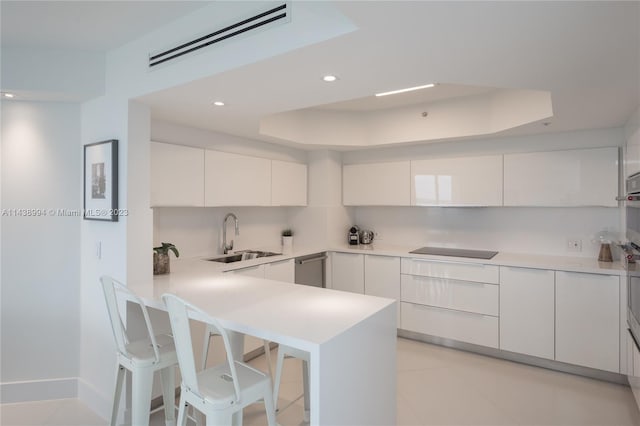 kitchen with sink, light tile floors, a tray ceiling, a kitchen bar, and white cabinetry