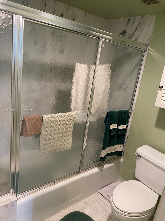 bathroom featuring toilet, tile flooring, and bath / shower combo with glass door