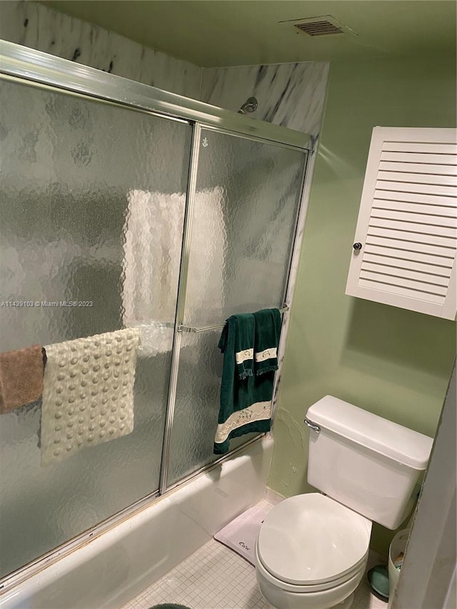 bathroom with tile floors, toilet, and bath / shower combo with glass door