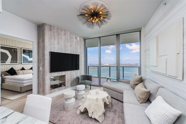 living room featuring a chandelier, a large fireplace, light hardwood / wood-style flooring, a water view, and a wall of windows