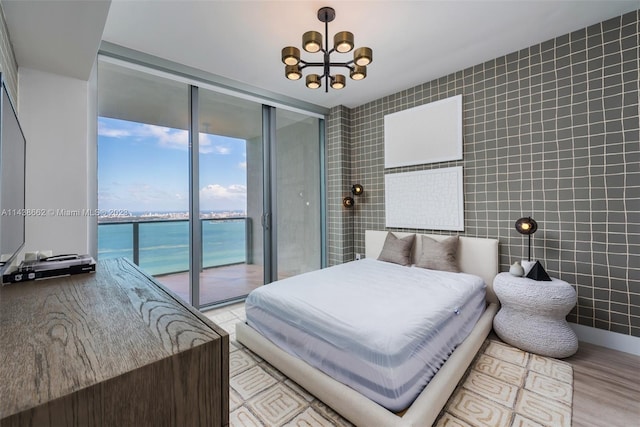 bedroom featuring tile walls, an inviting chandelier, a water view, and access to exterior