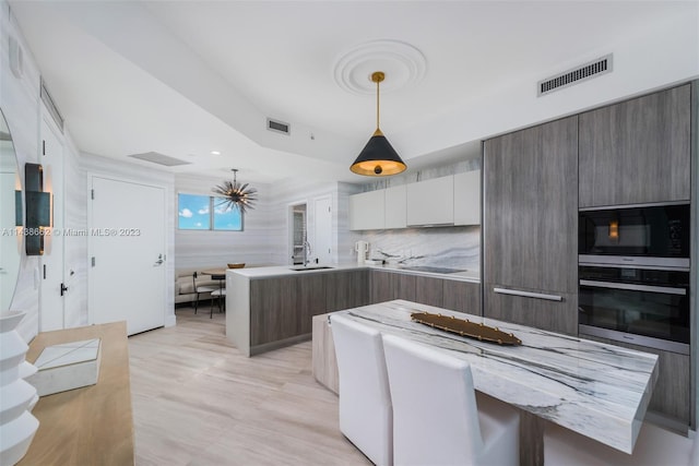 kitchen with sink, oven, light stone counters, hanging light fixtures, and black microwave