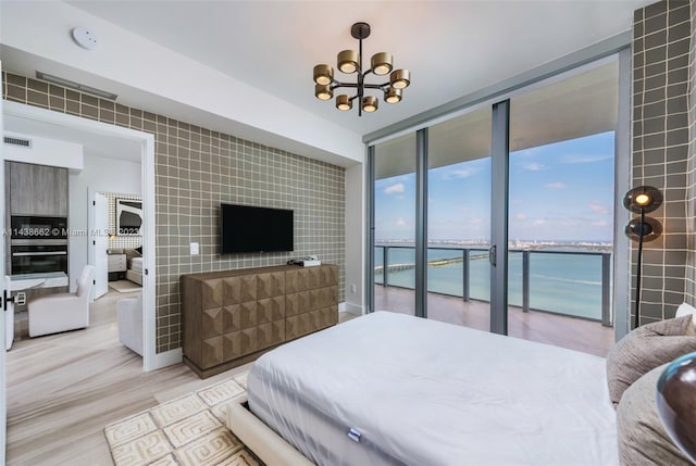 bedroom featuring expansive windows, access to outside, light hardwood / wood-style flooring, a water view, and a notable chandelier