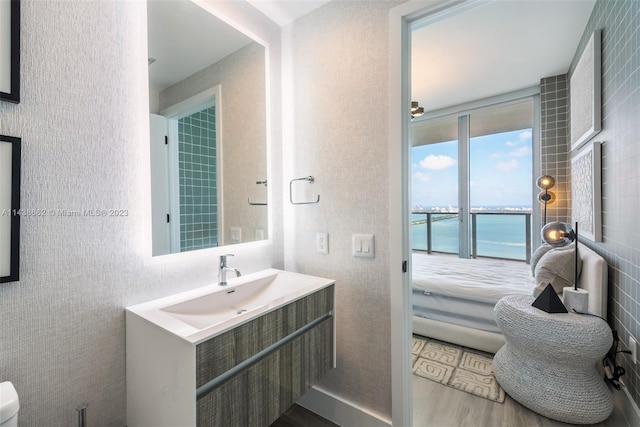 bathroom featuring tile walls, toilet, vanity with extensive cabinet space, wood-type flooring, and a water view