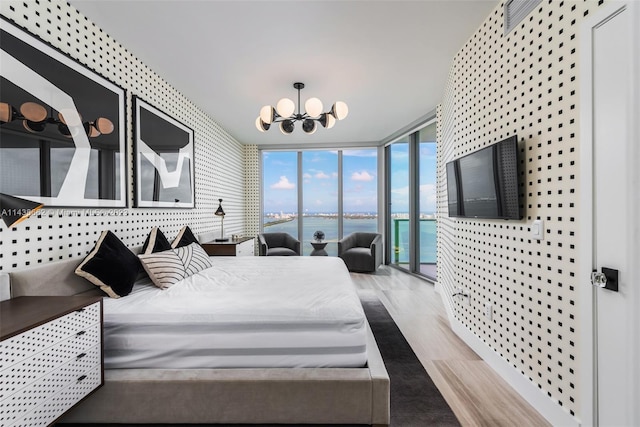 bedroom with access to exterior, expansive windows, a water view, light hardwood / wood-style floors, and an inviting chandelier