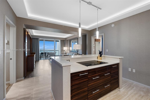 kitchen featuring pendant lighting, rail lighting, black electric stovetop, a raised ceiling, and light wood-type flooring