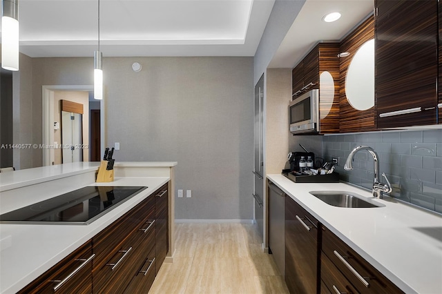 kitchen with sink, backsplash, light hardwood / wood-style floors, decorative light fixtures, and black electric stovetop