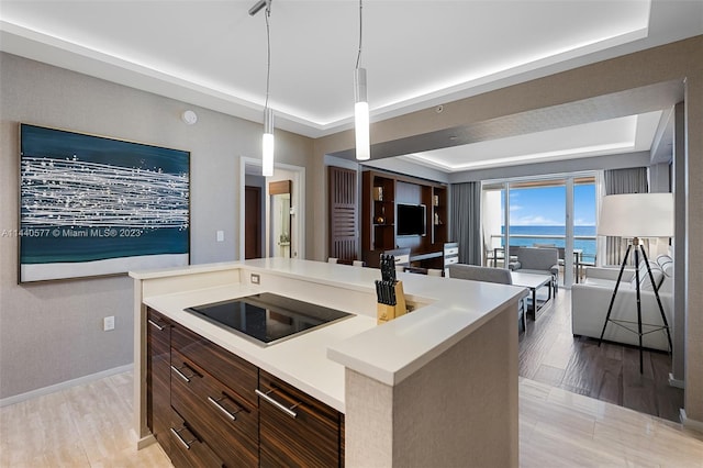 kitchen with pendant lighting, a kitchen island, light hardwood / wood-style floors, a tray ceiling, and dark brown cabinetry