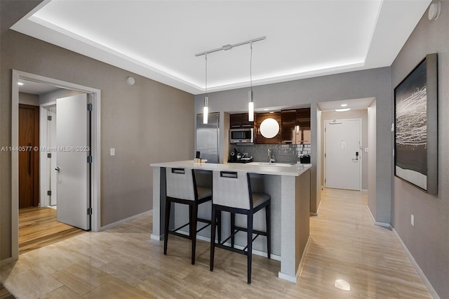 kitchen featuring pendant lighting, a kitchen bar, appliances with stainless steel finishes, backsplash, and a tray ceiling