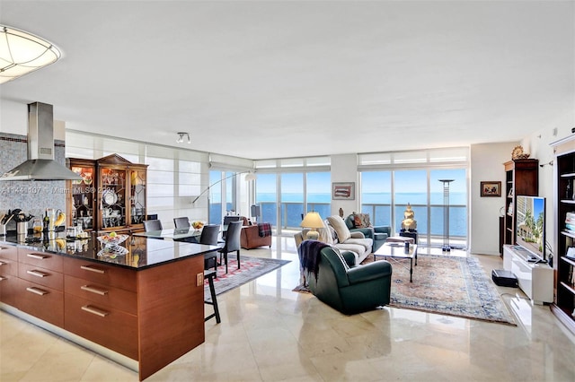 kitchen with expansive windows, light tile flooring, a water view, wall chimney range hood, and a kitchen bar