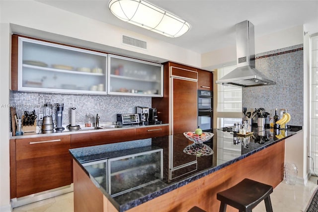 bar featuring tasteful backsplash, dark stone counters, wall chimney range hood, black double oven, and light tile floors