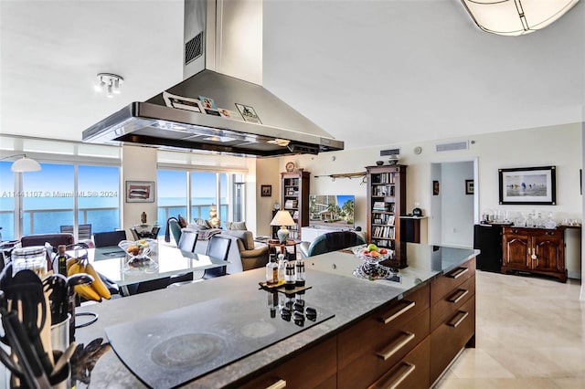 kitchen featuring a water view, dark stone counters, island range hood, and light tile floors