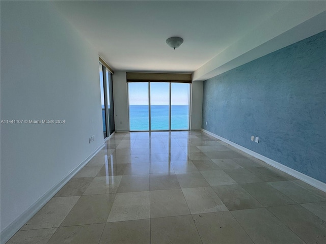 empty room with floor to ceiling windows, a water view, and light tile flooring