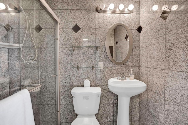 bathroom with tile walls, toilet, a shower with shower door, and sink