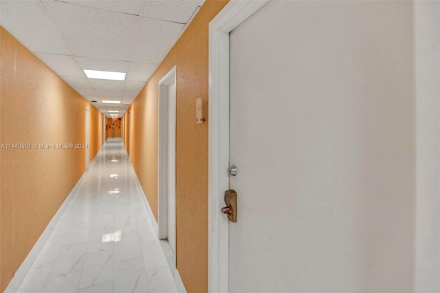 hall with light tile floors and a paneled ceiling