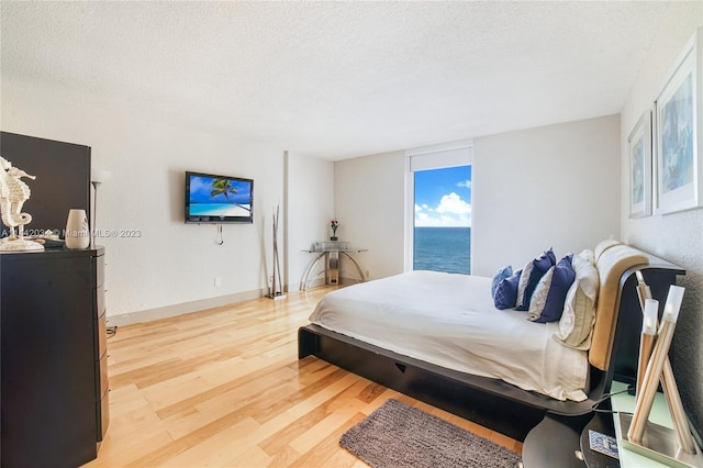 bedroom featuring a textured ceiling, light wood-type flooring, and a water view