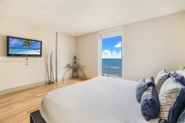 bedroom featuring a textured ceiling, a water view, and light hardwood / wood-style flooring