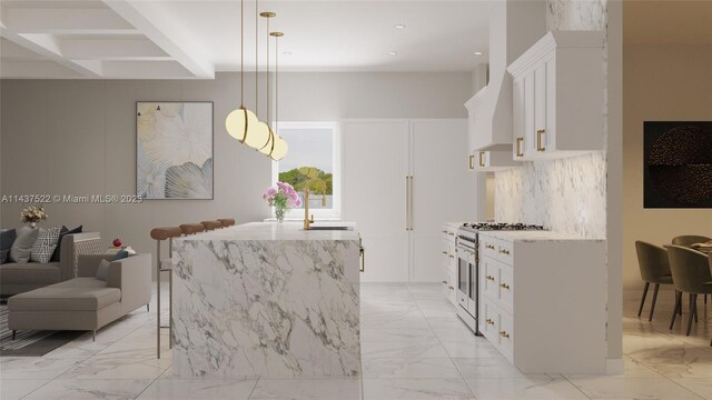 kitchen featuring sink, hanging light fixtures, white cabinets, a center island with sink, and range with two ovens