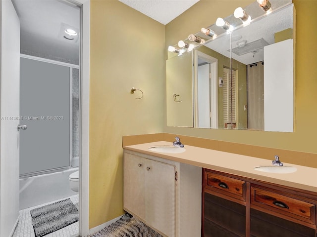 full bathroom featuring toilet, double sink, vanity with extensive cabinet space, shower / bath combination with glass door, and a textured ceiling