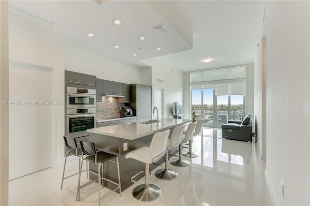 kitchen with light tile floors, gray cabinets, stainless steel double oven, backsplash, and sink