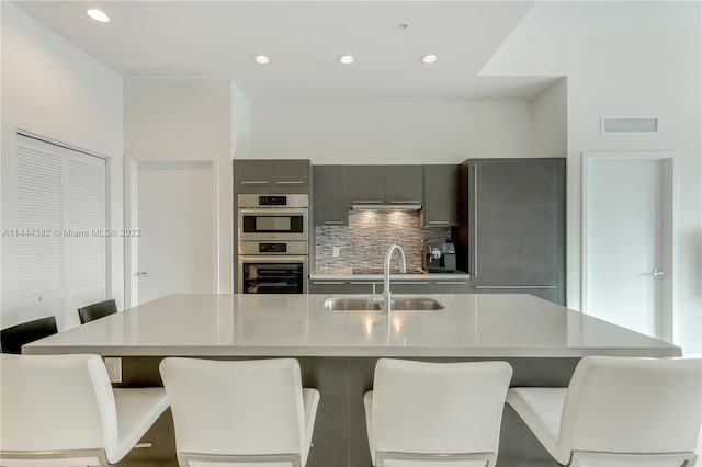 kitchen featuring gray cabinetry, double oven, a breakfast bar, sink, and tasteful backsplash