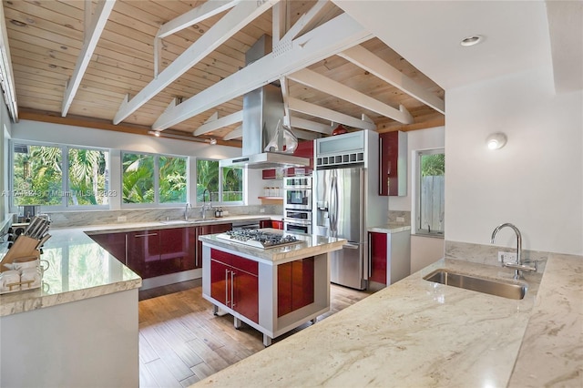 kitchen featuring appliances with stainless steel finishes, beam ceiling, island range hood, sink, and light stone counters