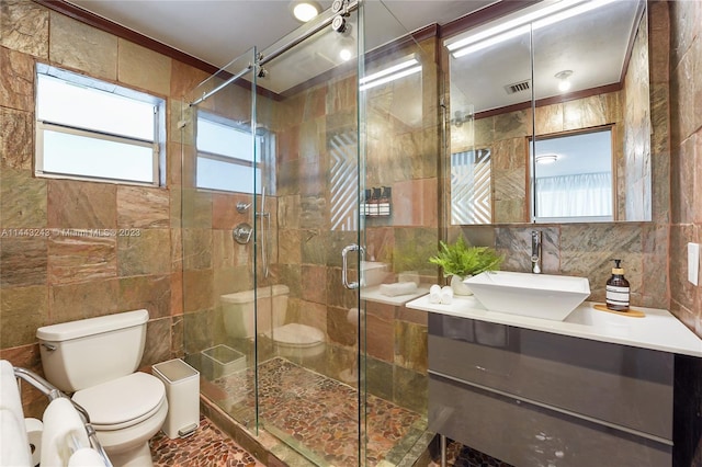 bathroom featuring a shower with door, backsplash, toilet, vanity, and tile walls