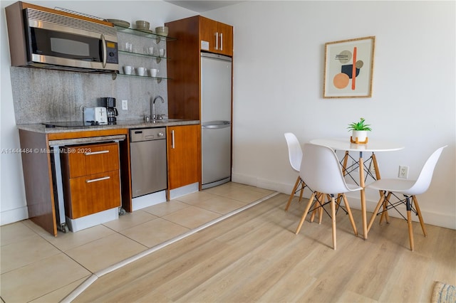 kitchen with stone counters, sink, light wood-type flooring, stainless steel appliances, and tasteful backsplash