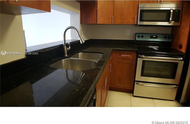 kitchen featuring light tile floors, dark stone counters, sink, and stainless steel appliances