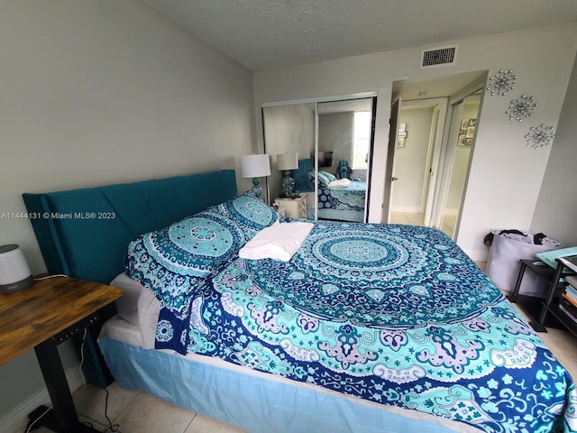 bedroom with a closet, a textured ceiling, and light tile floors