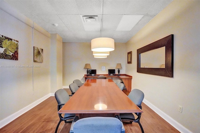 dining area featuring wood-type flooring and a drop ceiling