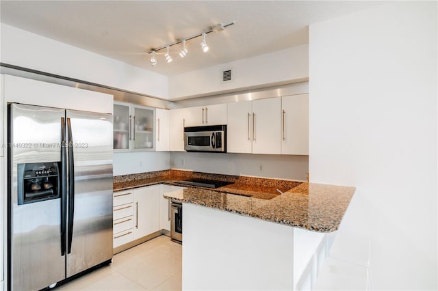 kitchen with kitchen peninsula, track lighting, stainless steel appliances, dark stone countertops, and white cabinets