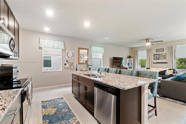 kitchen with ceiling fan, appliances with stainless steel finishes, a breakfast bar, sink, and a center island with sink