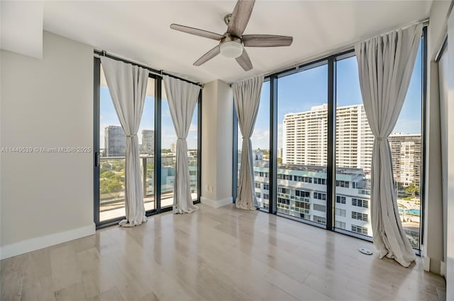 spare room with floor to ceiling windows, plenty of natural light, ceiling fan, and light wood-type flooring