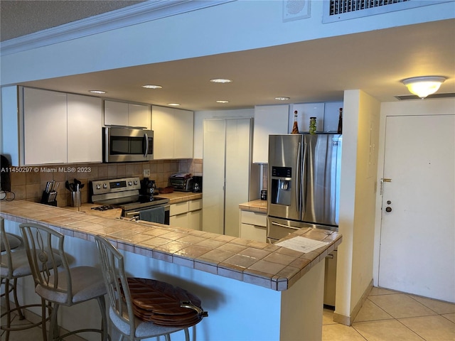 kitchen featuring tasteful backsplash, kitchen peninsula, appliances with stainless steel finishes, and white cabinetry