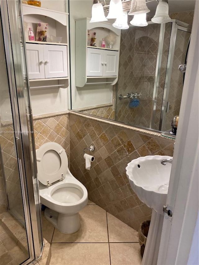 bathroom with tile floors, a shower with shower door, toilet, and tile walls