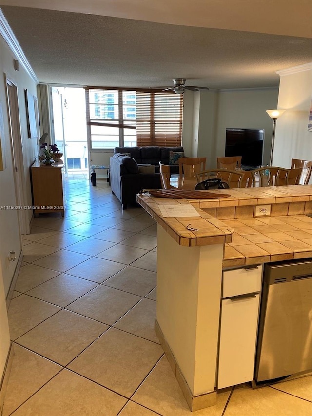 kitchen with expansive windows, ceiling fan, tile countertops, dishwasher, and ornamental molding