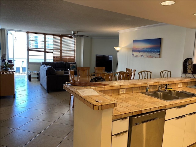 kitchen with ceiling fan, ornamental molding, white cabinets, tile counters, and dishwasher