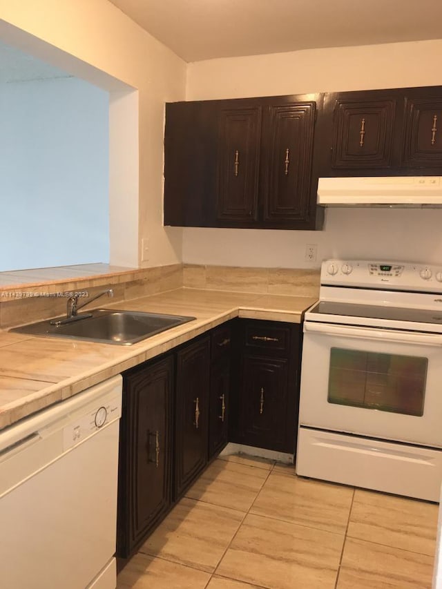 kitchen featuring white appliances, sink, light tile floors, wall chimney range hood, and dark brown cabinetry