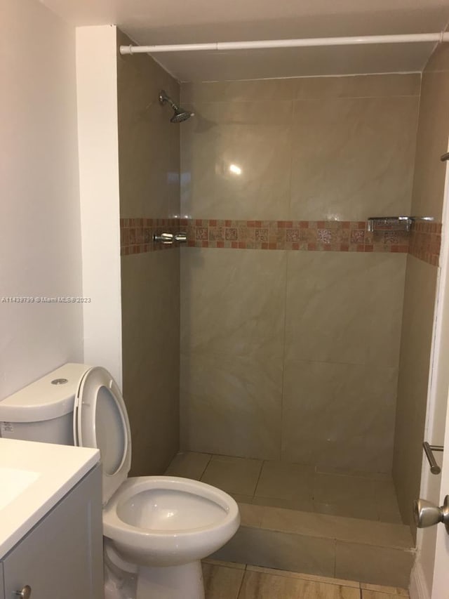 bathroom featuring vanity, a tile shower, tile flooring, and toilet