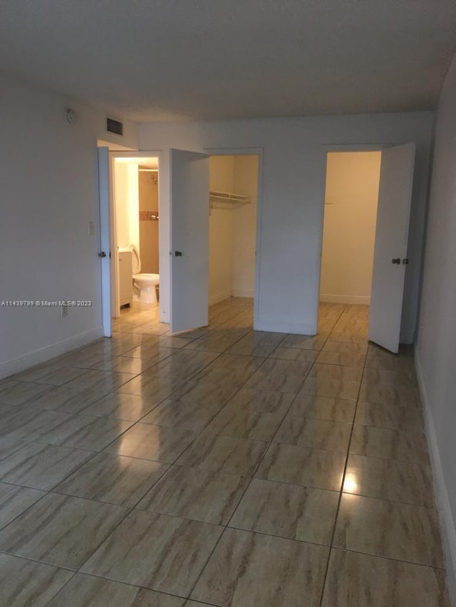 unfurnished bedroom featuring a closet, a spacious closet, ensuite bath, and light tile flooring