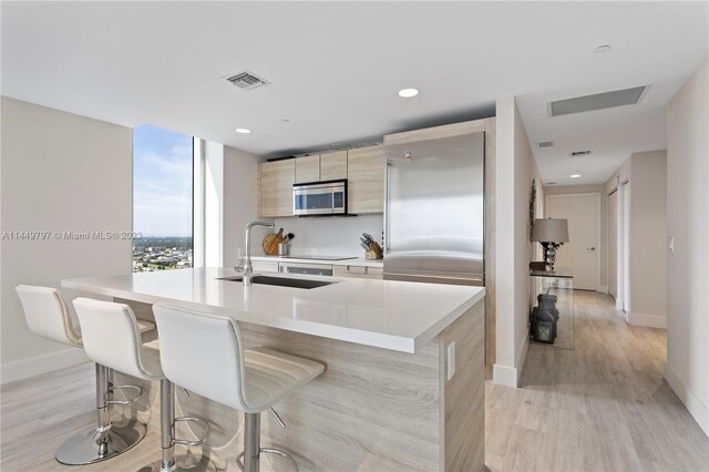 kitchen with light brown cabinets, light hardwood / wood-style floors, a kitchen breakfast bar, electric cooktop, and sink