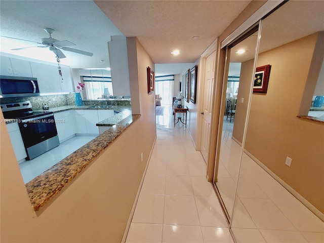 kitchen with light tile flooring, stainless steel appliances, ceiling fan, light stone countertops, and white cabinets