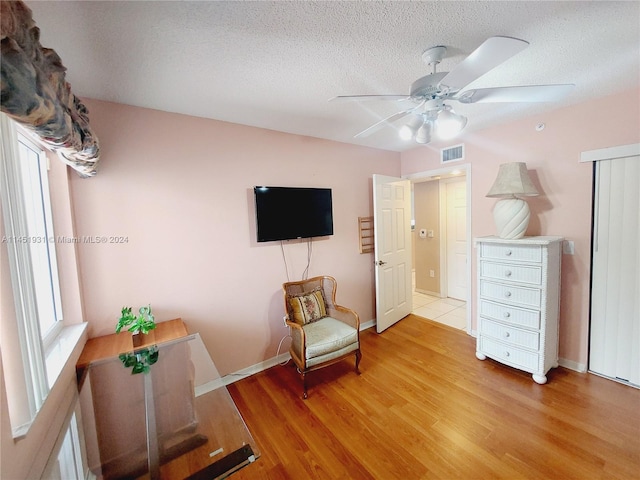 living area with a textured ceiling, light wood-type flooring, and ceiling fan