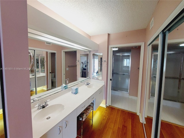 bathroom featuring dual sinks, toilet, large vanity, wood-type flooring, and a textured ceiling