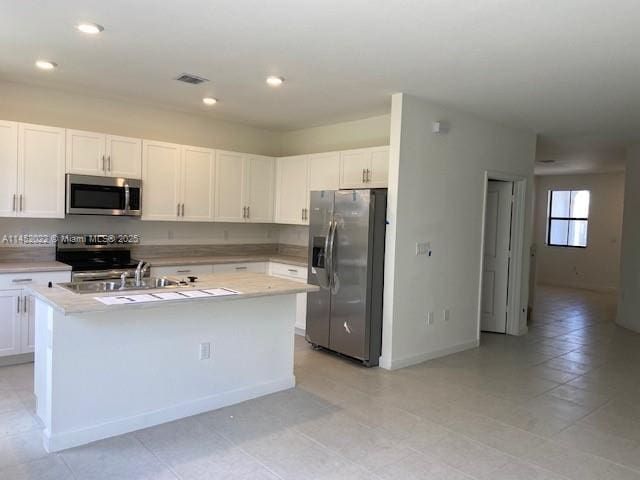 kitchen with white cabinets, a kitchen island with sink, light tile patterned floors, and stainless steel appliances